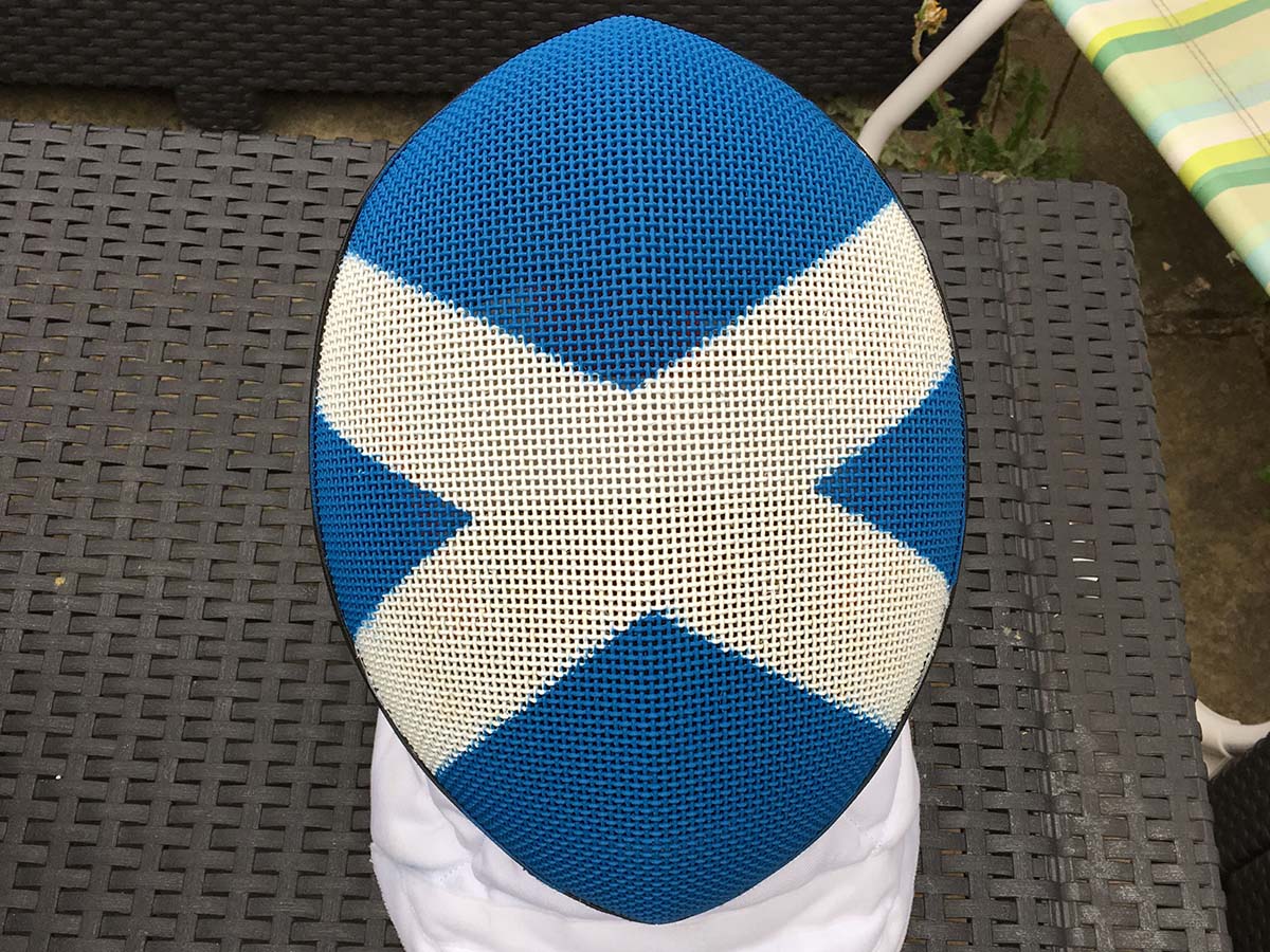 The Scottish fencing mask - sprayed and ready to go sitting on a garden table.